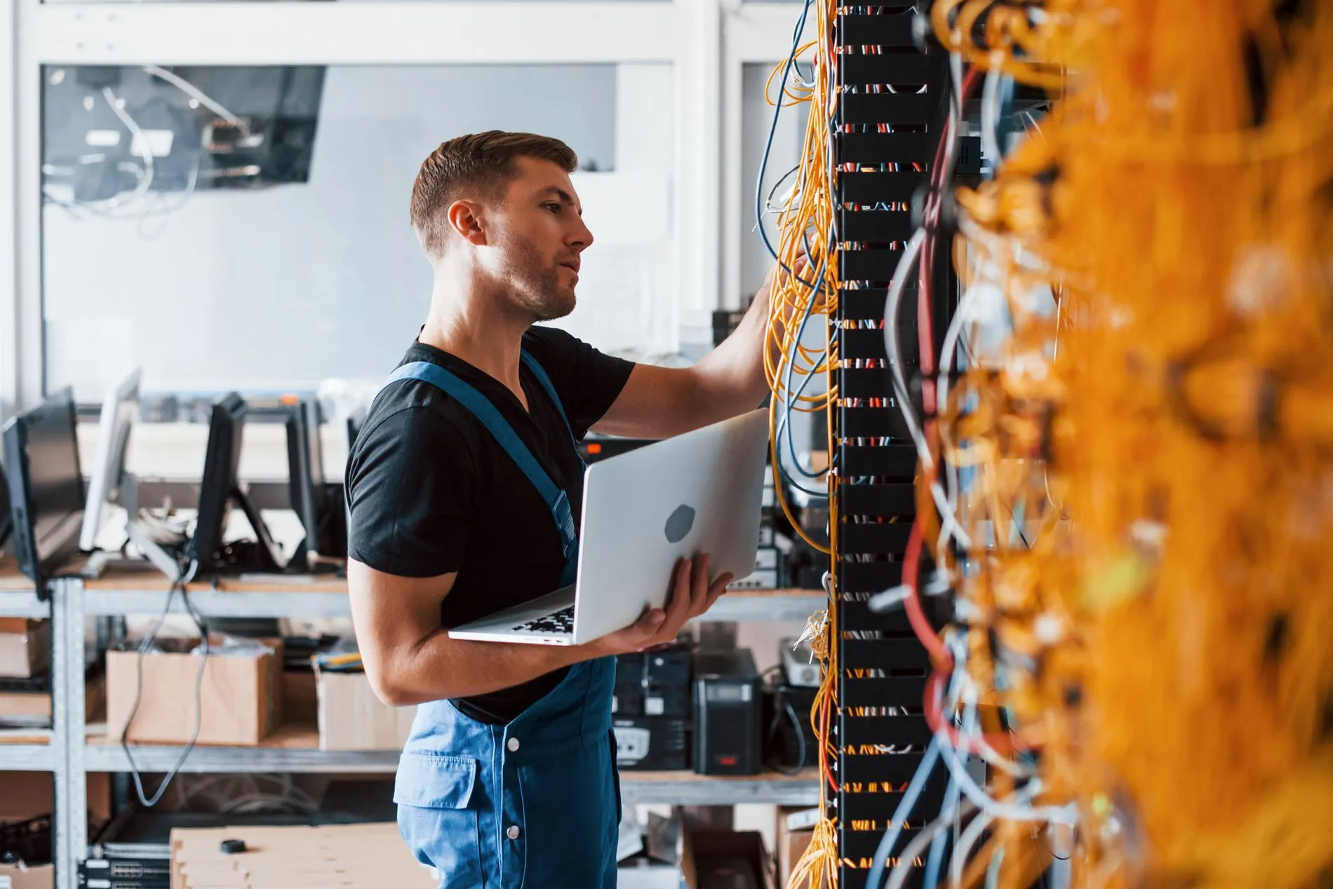 adobe_Young man in uniform and with laptop works with internet equipment and wires in server room